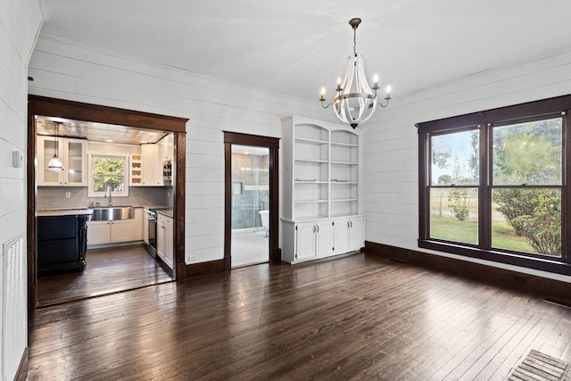 unfurnished dining area with wood walls, sink, a chandelier, and dark hardwood / wood-style floors