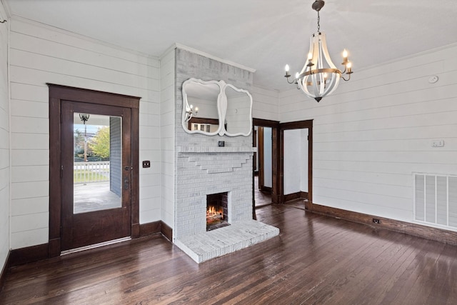 foyer featuring a brick fireplace, dark hardwood / wood-style floors, a notable chandelier, wood walls, and ornamental molding