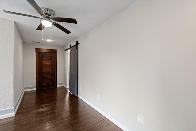 interior space with a barn door, ceiling fan, and dark wood-type flooring