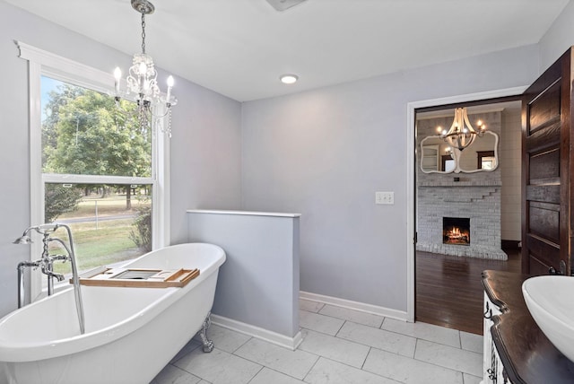 bathroom with vanity, an inviting chandelier, a bath, and a brick fireplace