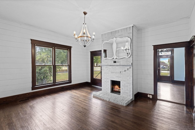 unfurnished living room featuring a brick fireplace, wooden walls, dark hardwood / wood-style floors, and an inviting chandelier