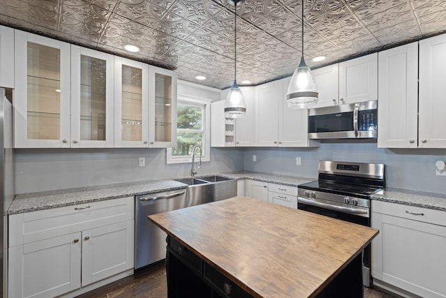 kitchen featuring white cabinetry, sink, stainless steel appliances, light stone counters, and decorative light fixtures