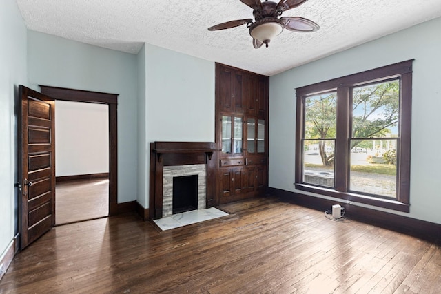 unfurnished living room with ceiling fan, a fireplace, dark wood-type flooring, and a textured ceiling