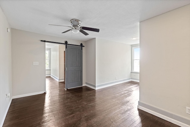 empty room with a barn door, ceiling fan, dark hardwood / wood-style flooring, and a textured ceiling