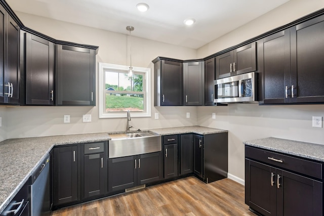 kitchen with pendant lighting, sink, light stone countertops, light wood-type flooring, and stainless steel appliances