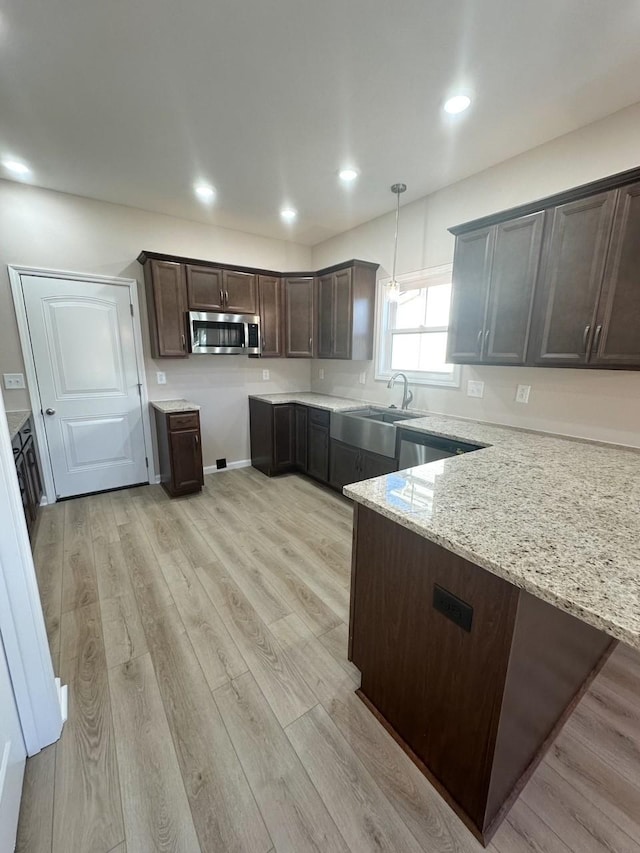 kitchen with dark brown cabinetry, light stone countertops, sink, hanging light fixtures, and light hardwood / wood-style flooring