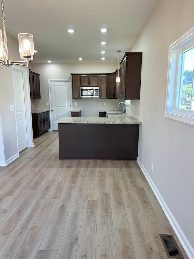 kitchen featuring pendant lighting, dark brown cabinetry, kitchen peninsula, and light hardwood / wood-style flooring