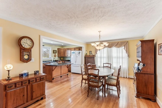 dining space featuring a healthy amount of sunlight, a textured ceiling, light hardwood / wood-style floors, and a notable chandelier