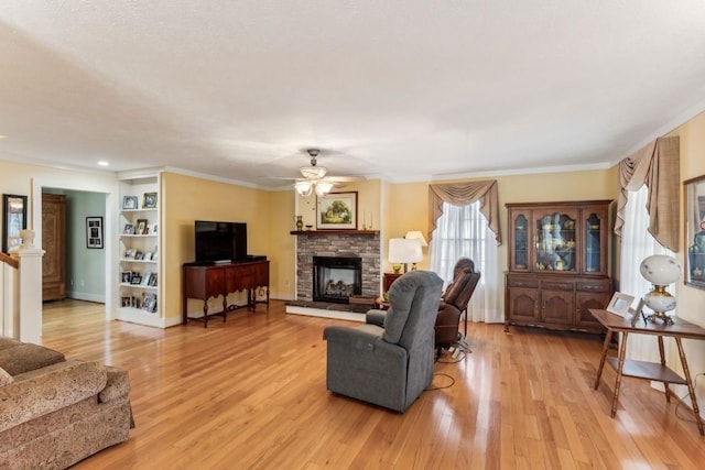 living room with light wood-type flooring, a stone fireplace, ceiling fan, and ornamental molding