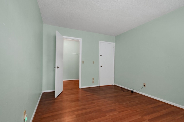 unfurnished bedroom with hardwood / wood-style floors, a textured ceiling, a spacious closet, and a closet