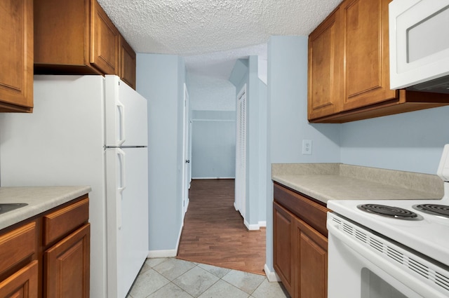 kitchen featuring white appliances, a textured ceiling, and light tile patterned floors