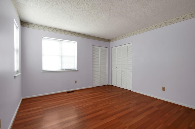 unfurnished bedroom featuring hardwood / wood-style floors, a textured ceiling, and two closets