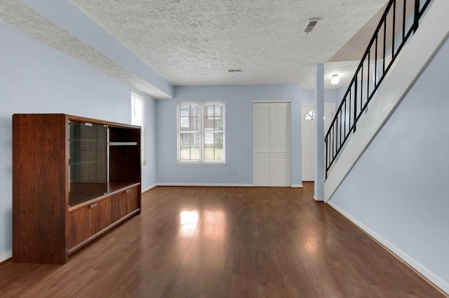 unfurnished living room featuring dark wood-type flooring and a textured ceiling