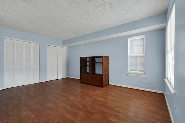 unfurnished bedroom featuring a textured ceiling, two closets, multiple windows, and dark wood-type flooring