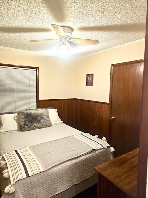 bedroom with a textured ceiling, crown molding, ceiling fan, and wooden walls