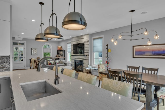 kitchen featuring sink, hanging light fixtures, light stone countertops, a fireplace, and a chandelier