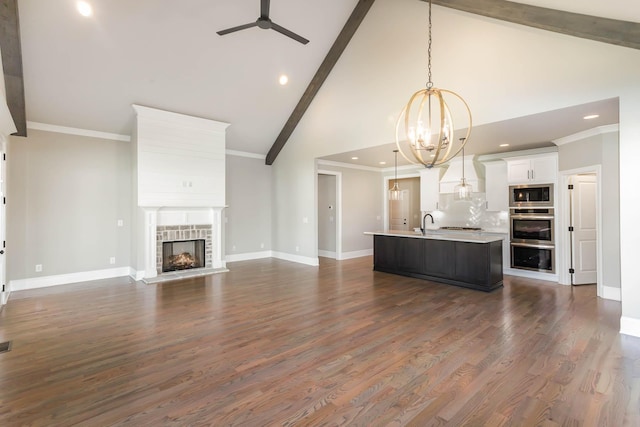 unfurnished living room featuring ceiling fan with notable chandelier, high vaulted ceiling, beamed ceiling, dark hardwood / wood-style floors, and a stone fireplace