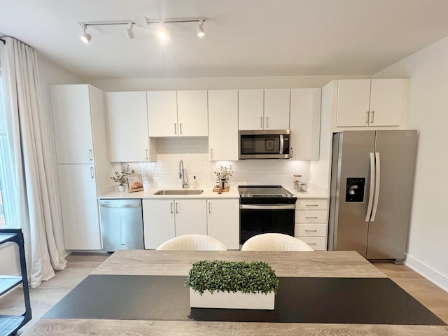 kitchen with sink, tasteful backsplash, light hardwood / wood-style flooring, white cabinets, and appliances with stainless steel finishes