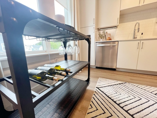 kitchen with decorative backsplash, stainless steel dishwasher, sink, light hardwood / wood-style flooring, and white cabinetry