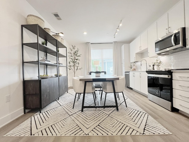 kitchen with tasteful backsplash, white cabinets, stainless steel appliances, and light hardwood / wood-style floors