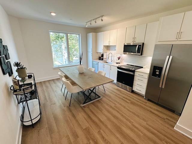 kitchen with backsplash, sink, light hardwood / wood-style flooring, appliances with stainless steel finishes, and white cabinetry