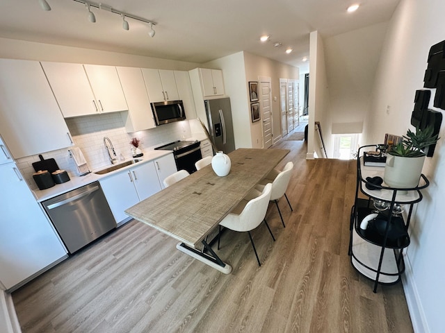 kitchen with appliances with stainless steel finishes, tasteful backsplash, sink, white cabinets, and light hardwood / wood-style floors