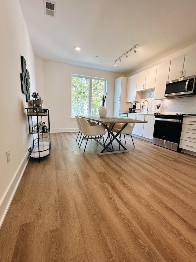 kitchen with rail lighting, stainless steel appliances, backsplash, light hardwood / wood-style floors, and white cabinets