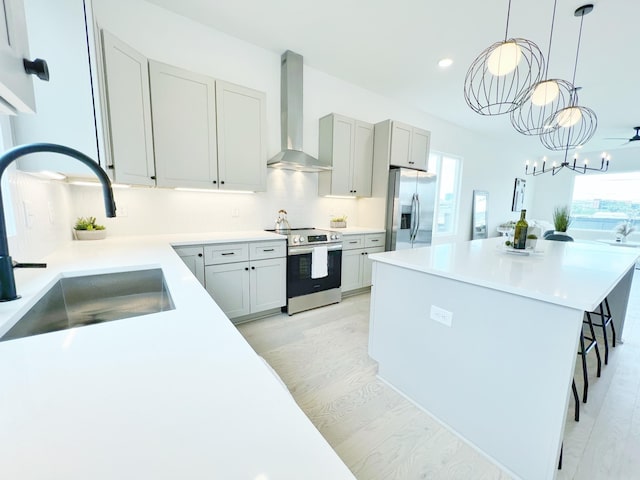 kitchen featuring wall chimney range hood, sink, light wood-type flooring, appliances with stainless steel finishes, and a breakfast bar area