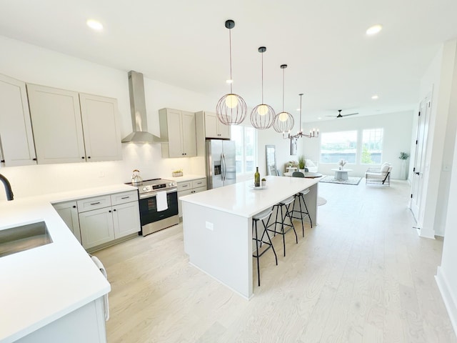 kitchen featuring a kitchen bar, appliances with stainless steel finishes, ceiling fan, wall chimney range hood, and a kitchen island