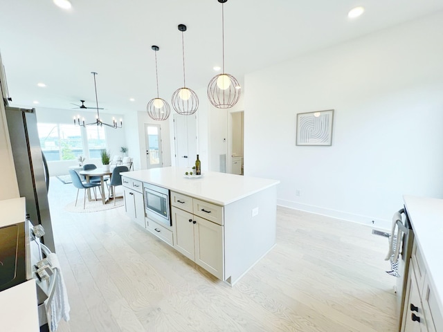 kitchen featuring light wood-type flooring, appliances with stainless steel finishes, a center island, and hanging light fixtures