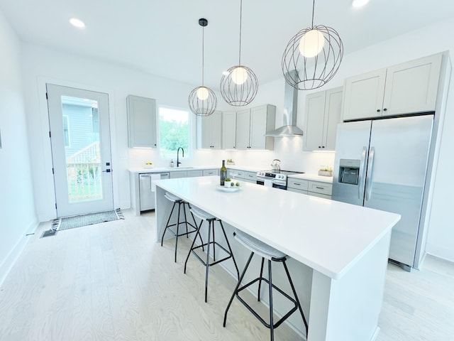 kitchen with wall chimney range hood, sink, a kitchen island, a kitchen bar, and stainless steel appliances