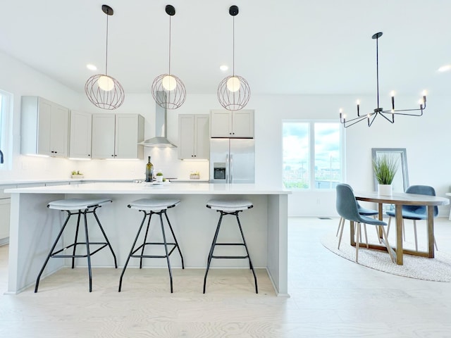 kitchen with stainless steel fridge with ice dispenser, decorative light fixtures, a large island, and wall chimney range hood