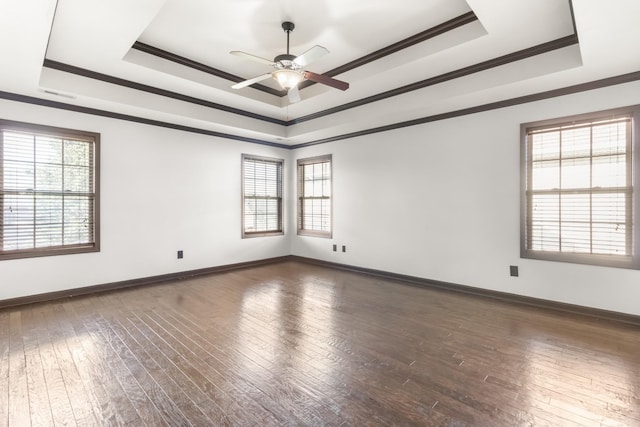 empty room with dark hardwood / wood-style floors, ceiling fan, a raised ceiling, and crown molding