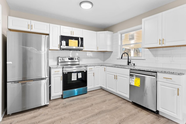 kitchen featuring sink, light hardwood / wood-style flooring, light stone countertops, appliances with stainless steel finishes, and white cabinetry