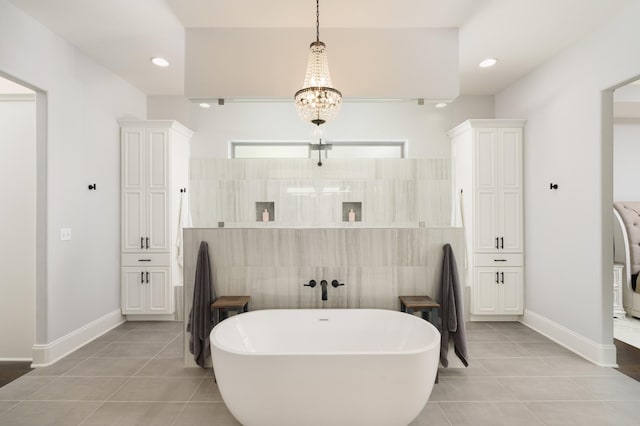 bathroom featuring an inviting chandelier, tile patterned floors, tile walls, and a bathing tub