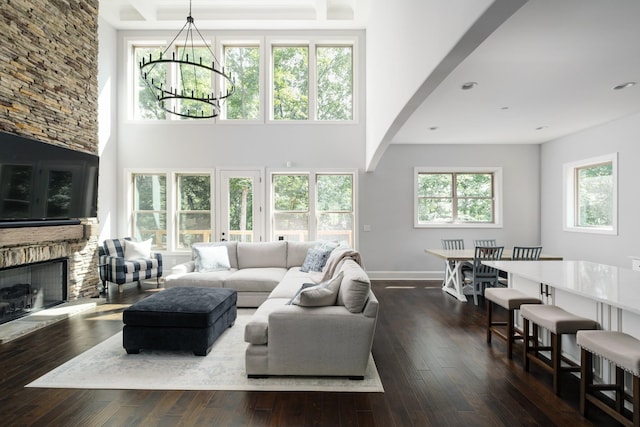 living room featuring a healthy amount of sunlight, an inviting chandelier, a stone fireplace, dark hardwood / wood-style flooring, and a towering ceiling