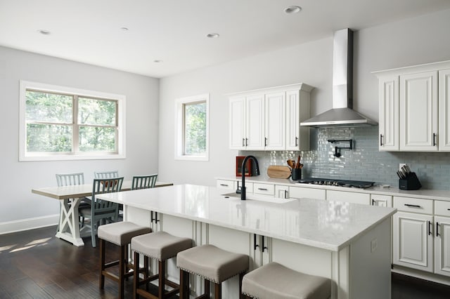 kitchen with white cabinetry, sink, wall chimney range hood, stainless steel gas stovetop, and a kitchen island with sink