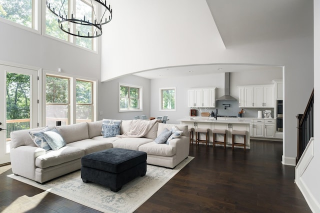 living room with dark hardwood / wood-style flooring, a towering ceiling, sink, and an inviting chandelier