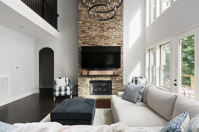 living room with a high ceiling, an inviting chandelier, a stone fireplace, and wood-type flooring