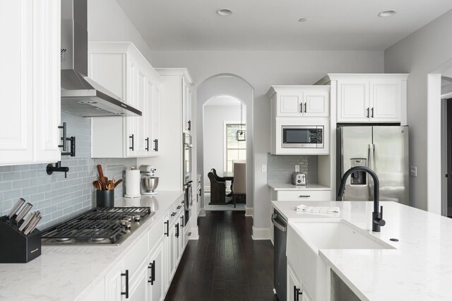 kitchen featuring light stone countertops, appliances with stainless steel finishes, sink, wall chimney range hood, and white cabinetry