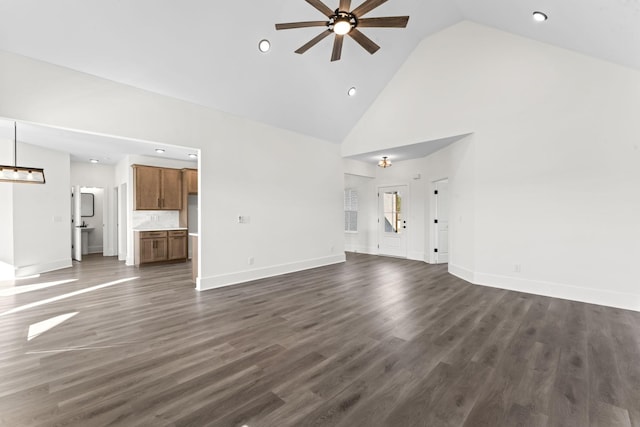 unfurnished living room with high vaulted ceiling, dark wood-type flooring, and ceiling fan with notable chandelier