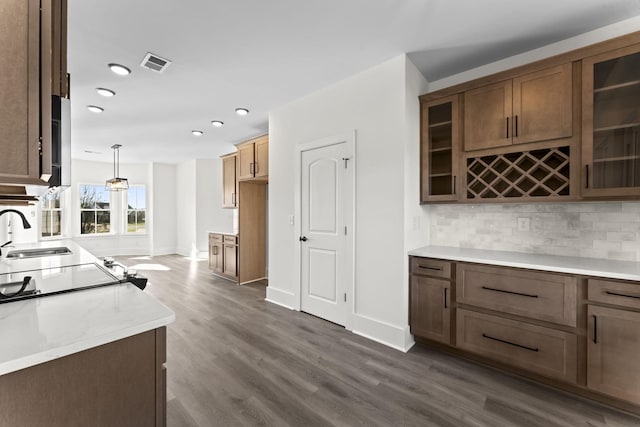 kitchen featuring tasteful backsplash, hanging light fixtures, dark wood-type flooring, and sink