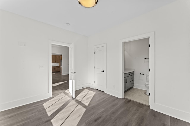 unfurnished bedroom featuring ensuite bath and dark wood-type flooring