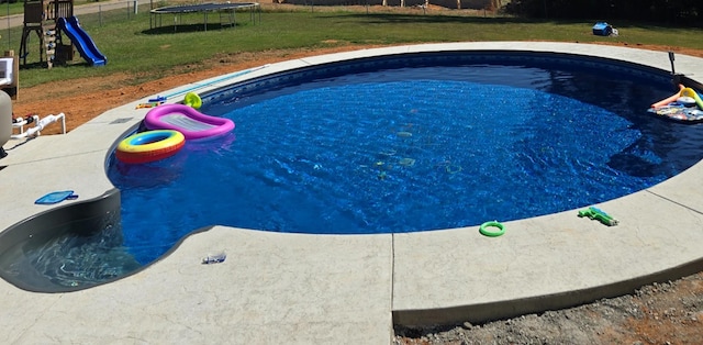 view of swimming pool featuring a playground, a yard, and a trampoline