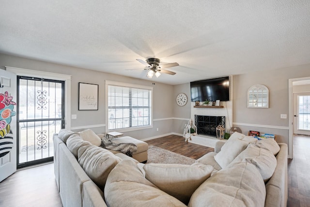 living room with ceiling fan, a large fireplace, a wealth of natural light, and light hardwood / wood-style flooring