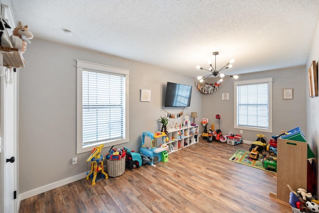 game room with hardwood / wood-style floors, a healthy amount of sunlight, and a notable chandelier