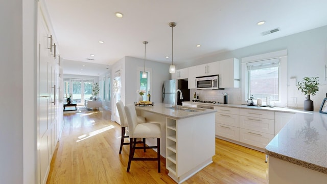 kitchen featuring white cabinets, pendant lighting, a center island with sink, and stainless steel appliances