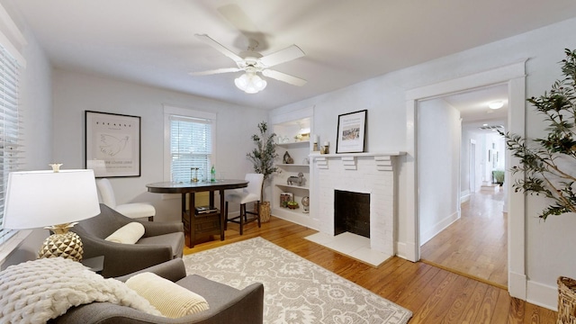 living room with a fireplace, built in shelves, light wood-type flooring, and ceiling fan