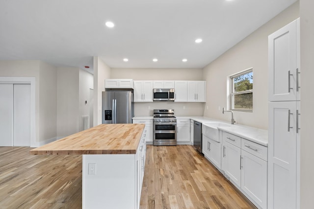 kitchen with appliances with stainless steel finishes, sink, a center island, butcher block countertops, and white cabinetry