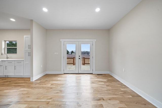 empty room with a healthy amount of sunlight, light hardwood / wood-style flooring, and french doors